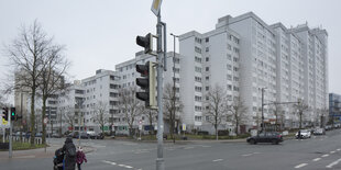 Eine Frau schiebt einen Kinderwagen über die Straße, im HIntergrund steht der Hochhauskomplex der "Grohner Düne"