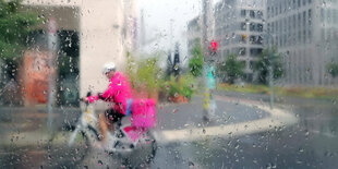 Ein Rider von Flink liefert im regen Lebensmittel aus.