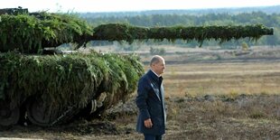 Olaf Scholz steht vor einem Leopard 2 Panzer, der mit grünen Ästen getarnt ist