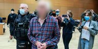 Der Angeklagte - der Vater des Hanau-Attentäters - wird von einem Polizisten in den Verhandlungssaal geführt