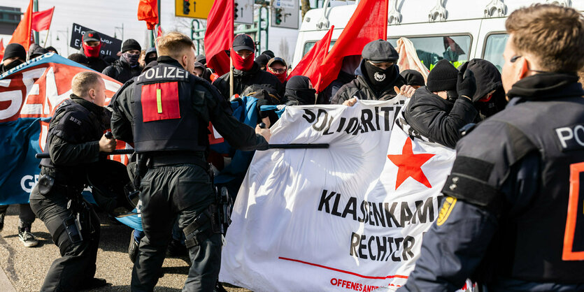 Beamte mit Schlagstöcken stehen Demonstrationsteilnehmern gegenüber, die Banner halten