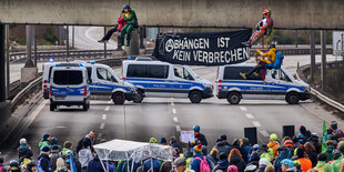 Menschen seilen sich von einer Autobahnbrücke ab, davor stehen Menschen und schauen zu