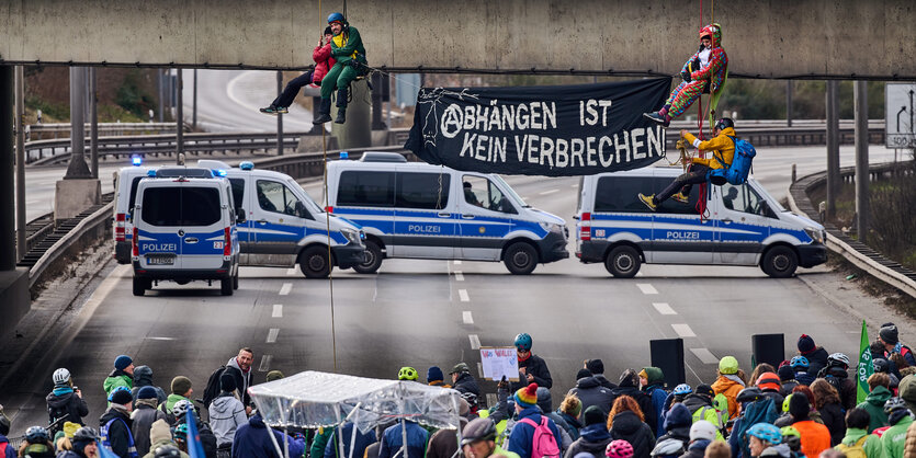 Menschen seilen sich von einer Autobahnbrücke ab, davor stehen Menschen und schauen zu