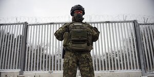 Ein bewaffneter Grenzschützer steht vor einer Grenzanlage an der polnisch-belarusischen grenze