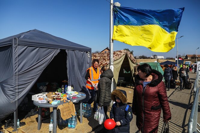 Menschen an einem Grenzübergang, im Hintergrund weht eine ukrainische Fahne