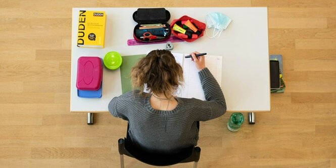 Blick von oben: Eine Schülerin sitzt während der Abiturprüfung an einem Tisch - darauf liegen ihre Bücher und Stifte