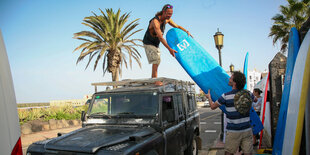 Zwei Männer laden Surfbretter ab von einem Land Rover