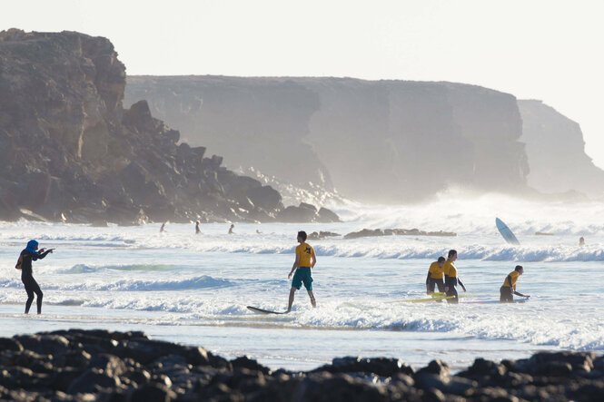 Surfer am Meer vor grandioser Vulkangesteinskulisse