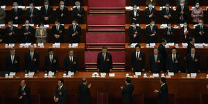 Ji Jinping steht am Redepult, umgeben von zahlreichen Menschen auf Rängen, die ihm applaudieren