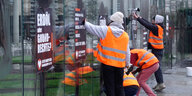 Menschen in Warnwesten kleben Plakate "Erdöl als Grundrecht" an eine spiegelnde Wand
