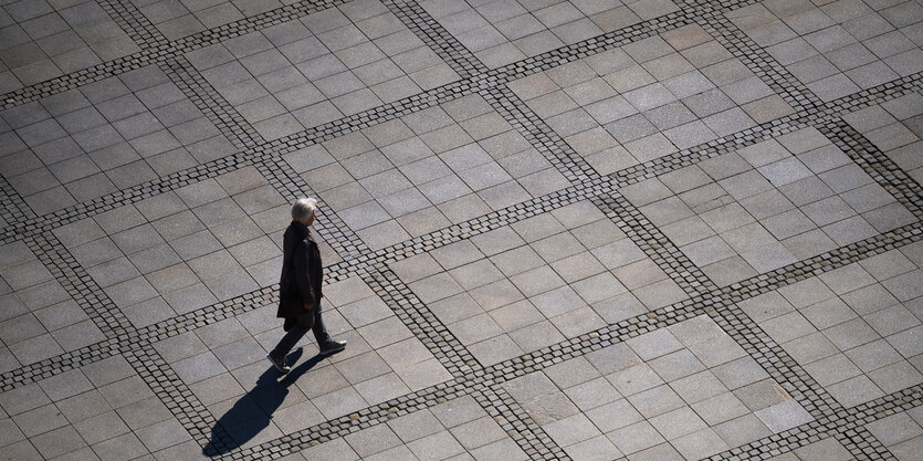 Eine Frau mit grauen von oben fotografiert, geht über einen leeren Marktplatz