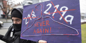 Eine Frau hält ein Transparent, auf dem steht: "218 129 - Never again"