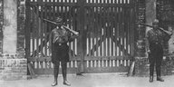 Zwei bewaffnete SA-Männer in Uniform stehen vor einem Holztor