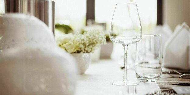 Ein festlich gedeckter Tisch, mit weißen Servietten und Tischtuch - in der Mitte steht ein leeres Sektglas