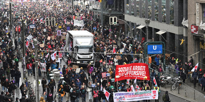 Ein Demonstrationszug in Berlin, zahlreiche Menschen auf einer Straße. Vorneweg tragen einige ein Banner mit der Aufschrift "Soziale Arbeit in die Offensive. Gute Löhne statt Inflation"