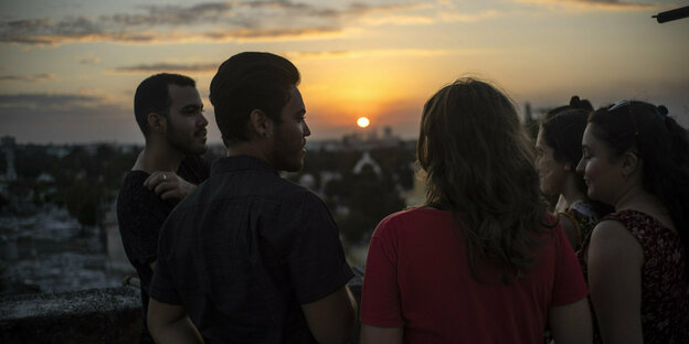 Junge Menschen stehen im Kreis, dahinter der Sonnenuntergang