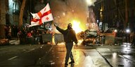 Ein Mann schwenkt eine georgische Fahne vor einer brennenden Barrikade