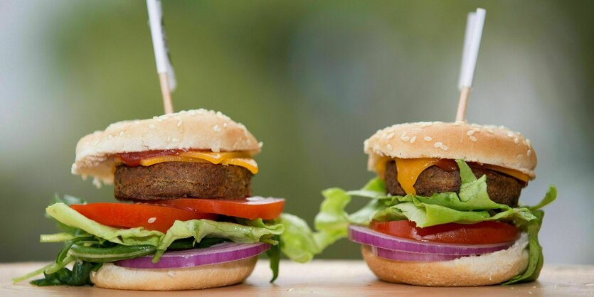 Zwei Insektenburger mit Salat und Tomate stehen auf einer Holzplatte