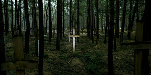 Helle Holzkreuze stehen zwischen den Bäumen in einem düsteren Wald
