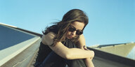 Die Musikerin Sara Persico sitzt auf einem angeschrägten Dach. Sie trägt eine Sonnenbrill und schaut hinunter.