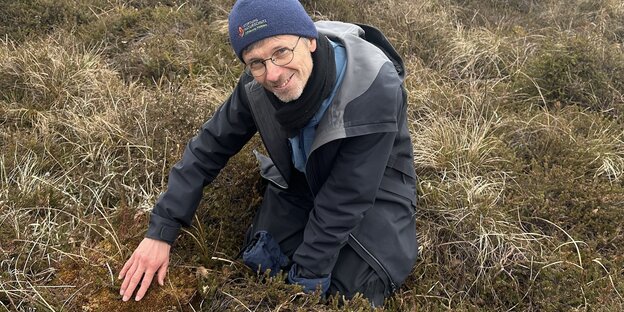 Der Botaniker Christian Dolnik sitz im Moor und streicht mit einer Hand über einen Hügel aus Moos