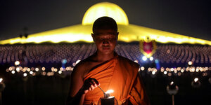 Ein buddhistischer Mönch zündet vor dem Wat Phra eine Kerze an.