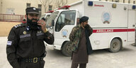 Polizist mit Funkrerät und Kämpfer der Taliban mit Kalaschnikow stehen vor einem Krankenhaus in Masar-e Scharif, in das Opfer des Anschlags gebracht wurden