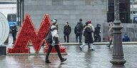 Menschen gehen im Schneetreiben an einem großen und roten Metro-Logo vorbei