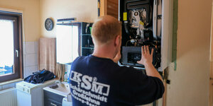 Ein Mitarbeiter einer Sanitär- und Heizungsbaufirma installiert eine moderne Gasbrennwerttherme in einem Einfamilienhaus