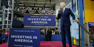 Joe Biden steht auf einer Bühne, die mit "Investieren in Amerika"-Schildern geschmückt ist
