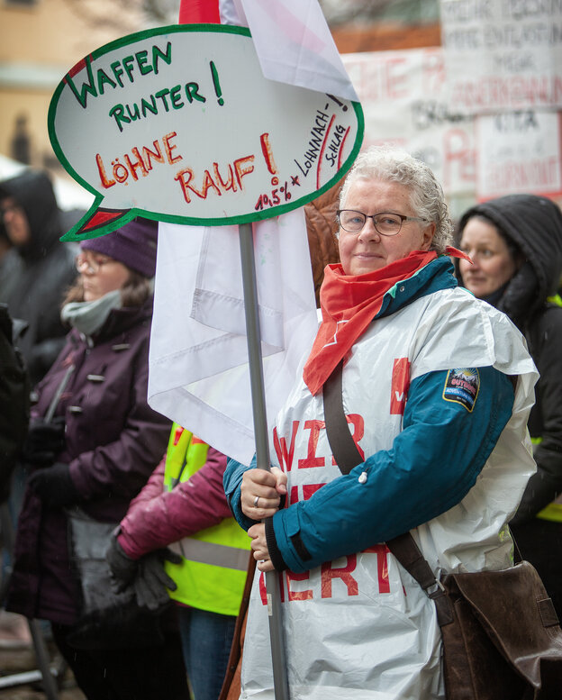 Eine weißhaarige Frau mit einem Protestplakat