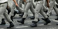 Soldaten in grauen Hosen und schwarzen Steifeln gehen im Gleichschritt auf der Straße