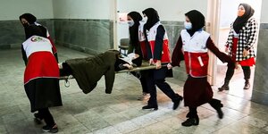 Sanitäterinnen tragen eine Bahre, auf der ein bewusstloses Mädchen liegt