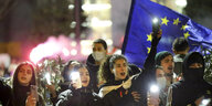 Junge Menschen leuchten mit ihren Smartphones, im Hintergrund eine Flagge der EU