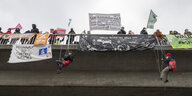 Aktivisten seilen sich von einer Autobahnbrücke in Frankfurt ab. Auf der Brücke stehen Menschen mit Transparenten und Protestschildern.