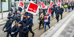 Menschen in blauer Dienstkleidung protestieren gemeinsam mit Verdi-Flaggen in der Hand