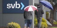 Menschen mit Regenschirm laufen an Firmenlogo der SVB vorbei