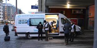 Blick in das beleuchtete Arztmobil, das in einer Unterführung steht. Zwei Helfer sprechen mit Menschen vor dem Arztmobil