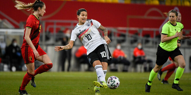 Dzsenifer Marozsán spielt den Ball, links Gegenspielerin, rechts Schiedsrichterin