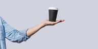 Eine Hand balanciert einen Einmal-Kaffeebecher