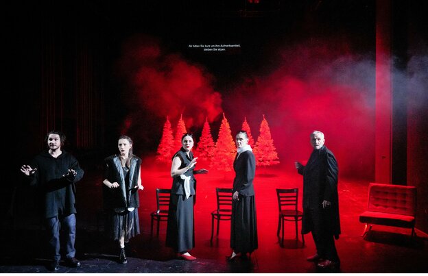 Vor roten Bäumen stehen fünf Schauspieler:innen auf der Bühne