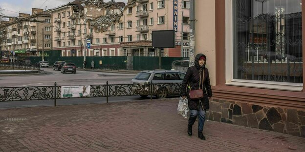 eine Frau im Wintermantel geht durch eine Straße, in der ein von Bomben getroffenes Gebäude steht. Auf dem Gebäude die Aufschrift: Hotel Ukraine