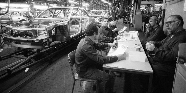 Arbeiter in einem Autowerk machen eine Pause neben dem Fliessband