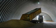 Ein Kipplaster entlädt Getreide in einer großen gewölbten Halle