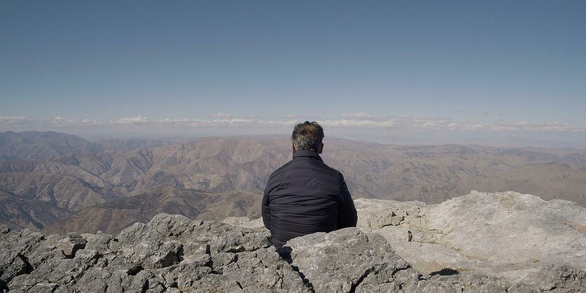 Ein Mann, dessen Rücken man sieht, schaut in eine weite Berglandschaft