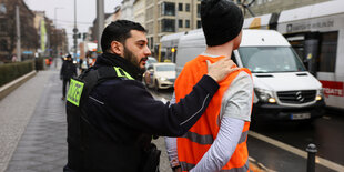 Das Bild zeigt einen Polizisten wie er einen Aktivist der Letzten Generation abführt