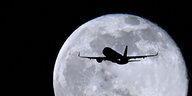 Eine Silhouette eines fliegenden Flugzeugs. Im Hintergrund der Mond