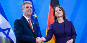 Annalena Baerbock und Eli Cohen reichen sich die Hand, im Hintergrund die Flaggen Israels, Deutschlands und der EU