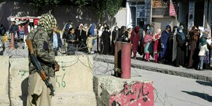 Ein bewaffneter Taliban steht vor einer Absperrung mit Stacheldraht und beobachtet die Menschen, die am Passamt anstehen