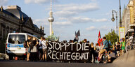 Eine Straße in Berlin. Menschen halten eine schwarze Fahne mit der Aufschrift "Stoppt die rechte Gewalt" in Großbuchstaben.
